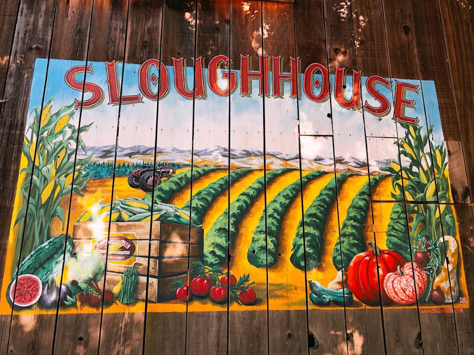 A hand-painted mural reading 'Sloughhouse' with corn, pumpkins, and farm produce, near the Rancho Murieta produce stands